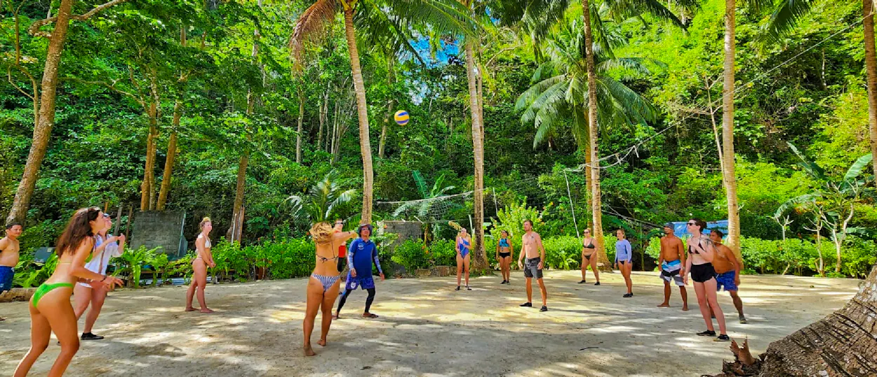 Energetic backpackers playing volleyball on a sandy court surrounded by lush palm trees at Island Camp.
