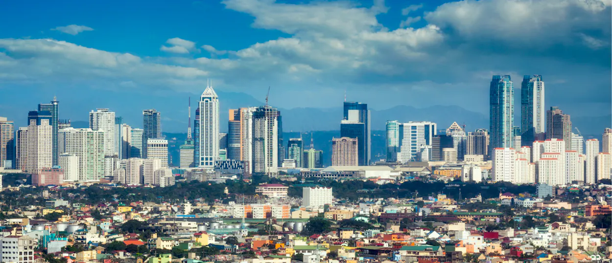 Panoramic view of a bustling city with colorful low-rise buildings and a skyline of modern skyscrapers.
