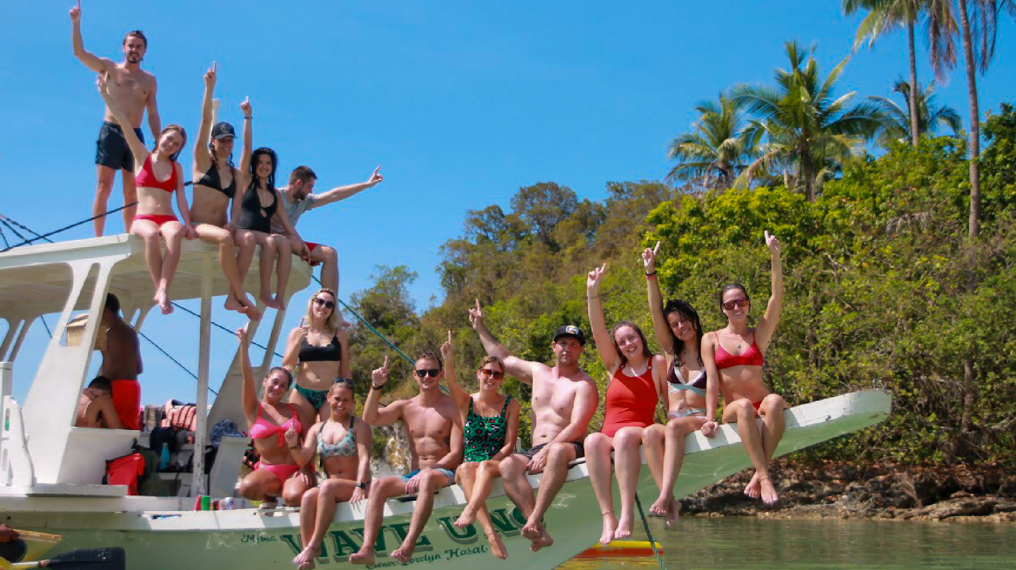 A group of excited backpackers on a boat trip in the sunny Philippines, raising their arms.