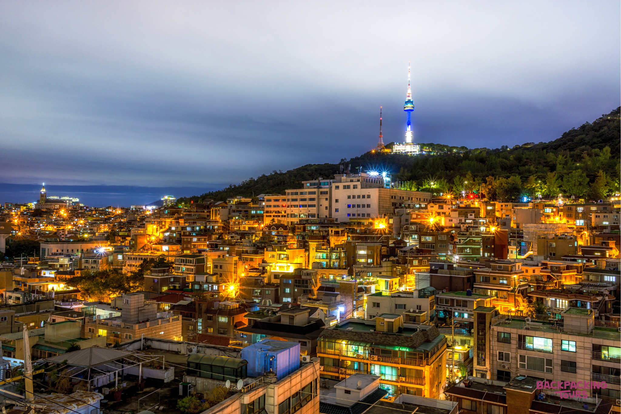 A vibrant night view of Seoul city with Namsan Tower glowing blue and white.