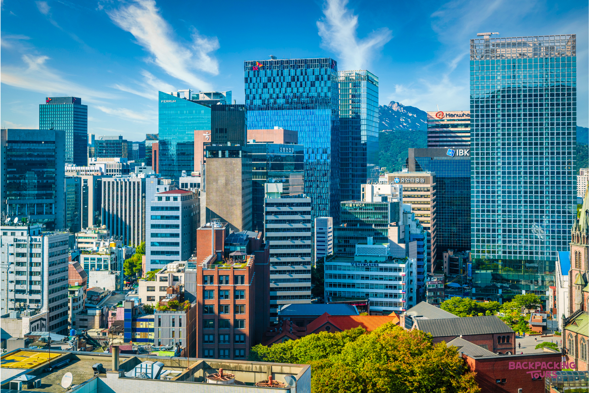 Vibrant cityscape of Seoul, showcasing modern skyscrapers, diverse buildings, and distant mountains under a blue sky.