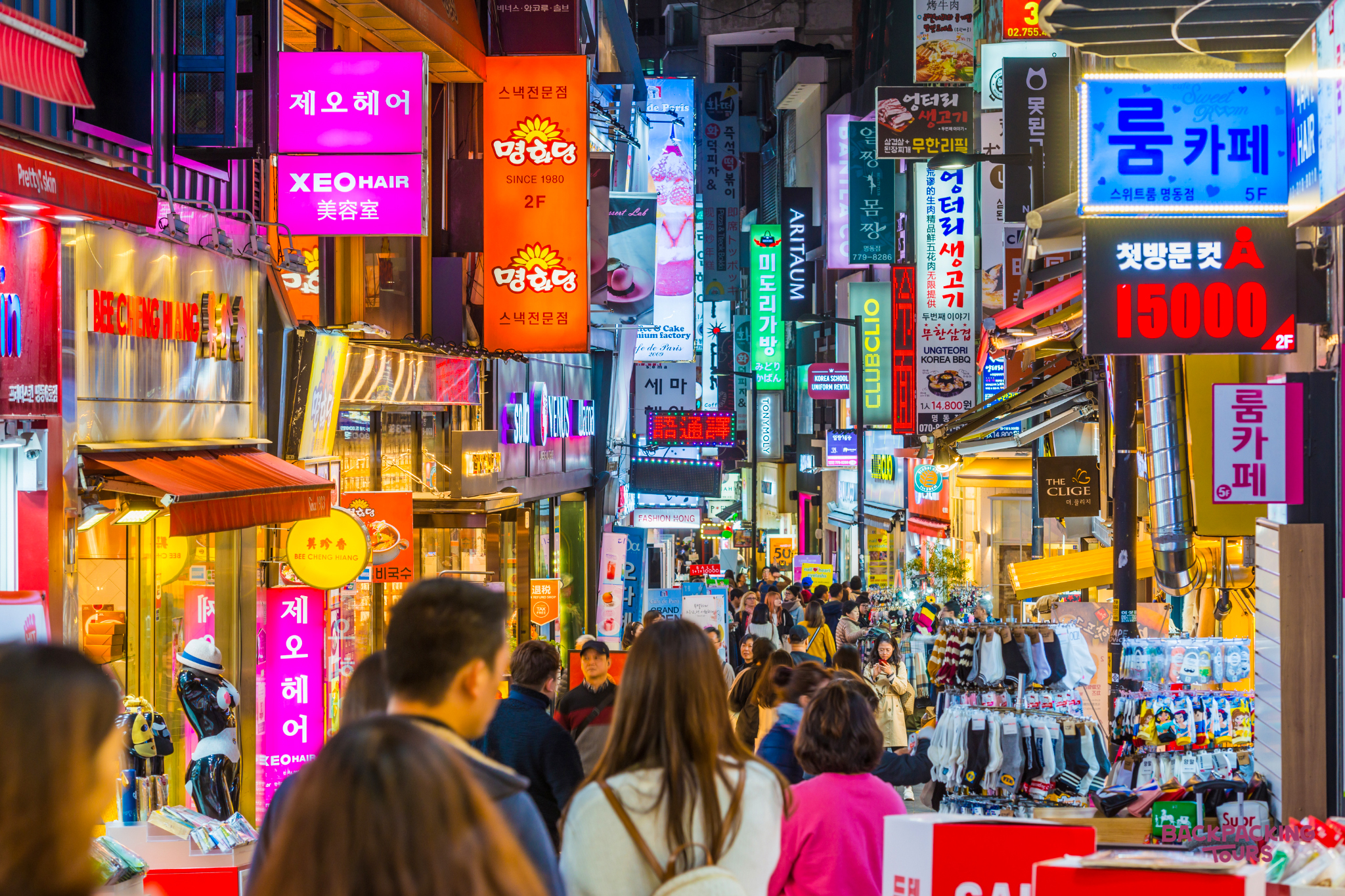 A vibrant street in Myeongdong, Seoul, bustling with people and colorful neon signs at night.