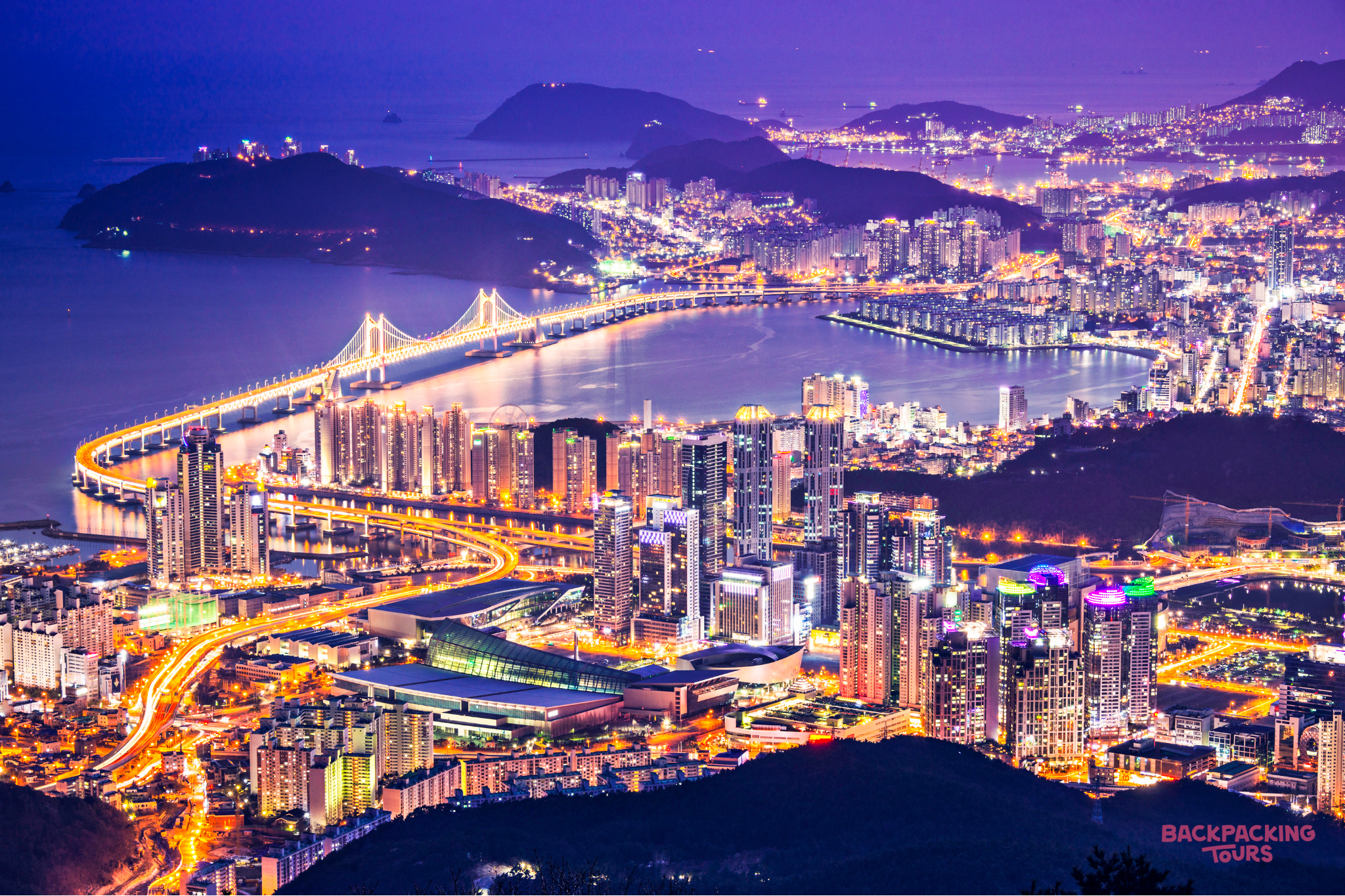 A breathtaking night view of Busan, South Korea, with the illuminated Gwangan Bridge and city lights.