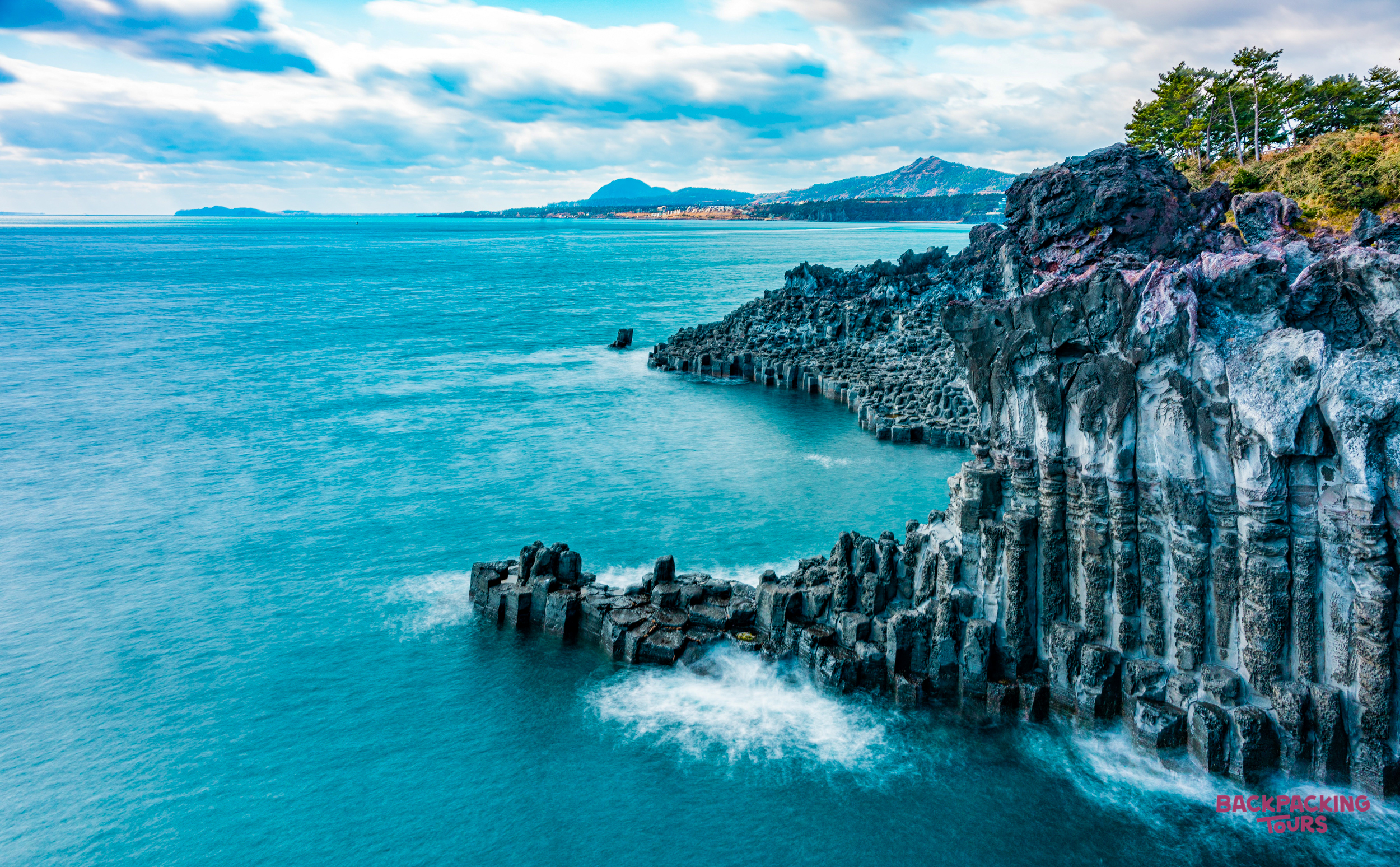 Dramatic hexagonal basalt columns of Jusangjeolli Cliff on Jeju Island meet the turquoise ocean.