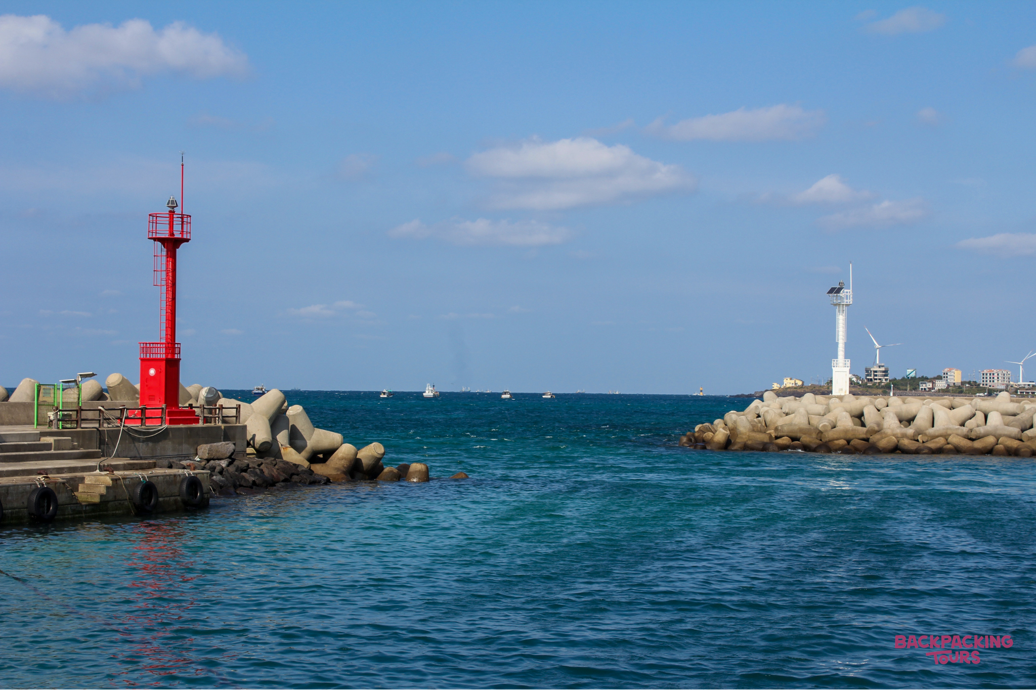 Red and white lighthouses on concrete breakwaters frame the entrance to a harbor on Jeju Island.