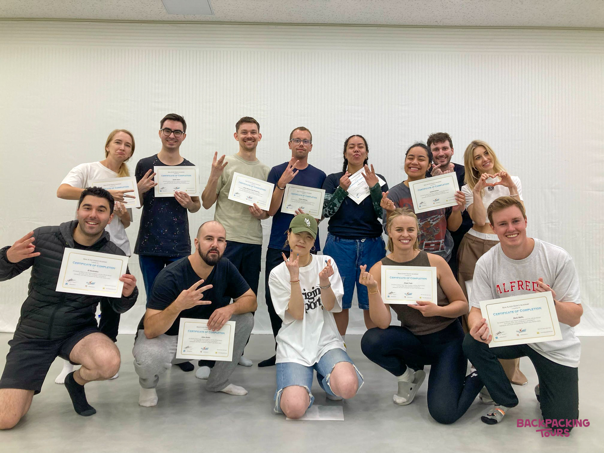 A group of happy backpackers proudly display their K-pop dance class certificates in Seoul.