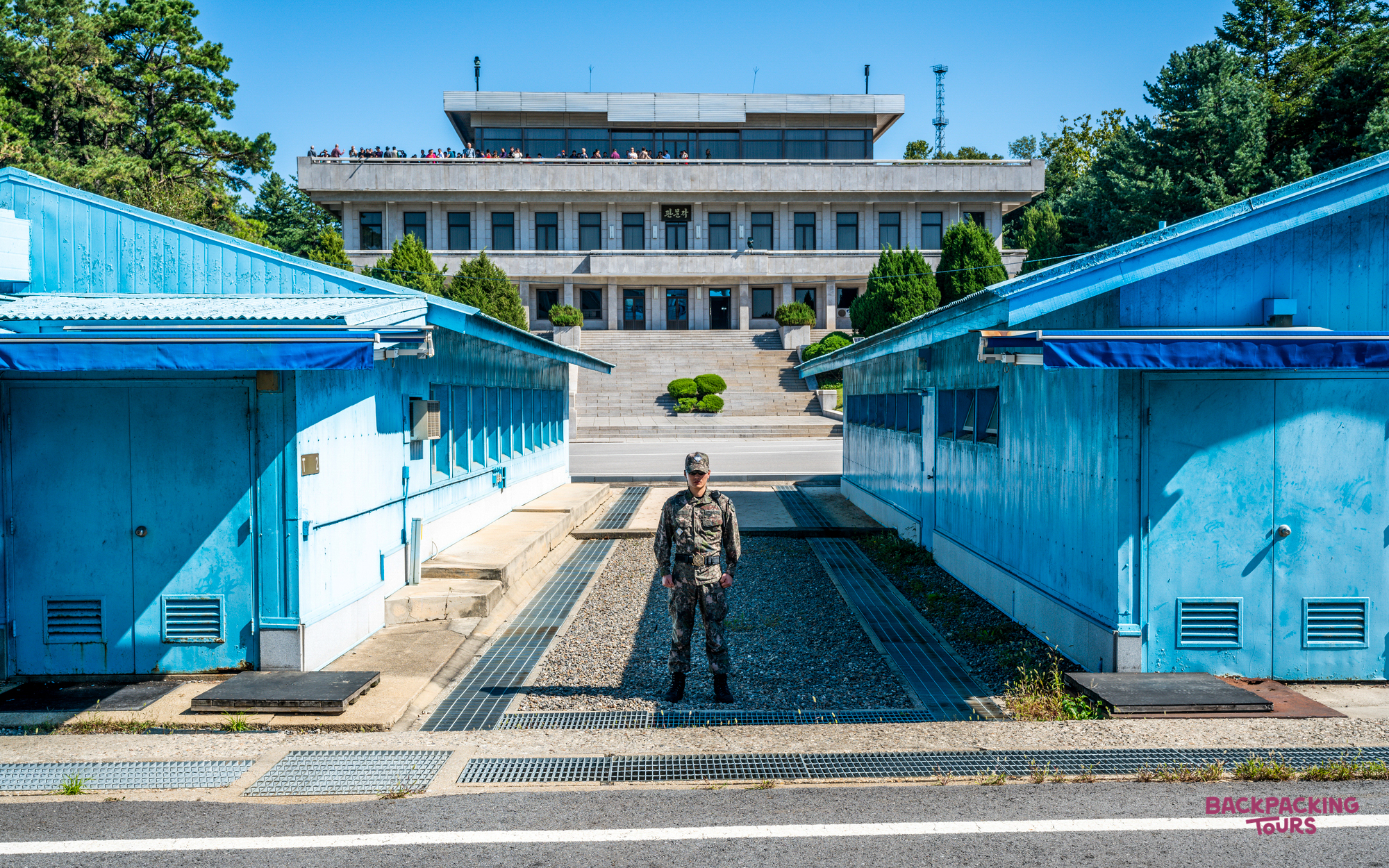 A soldier in camouflage stands between blue buildings at the Demilitarised Zone, South Korea.