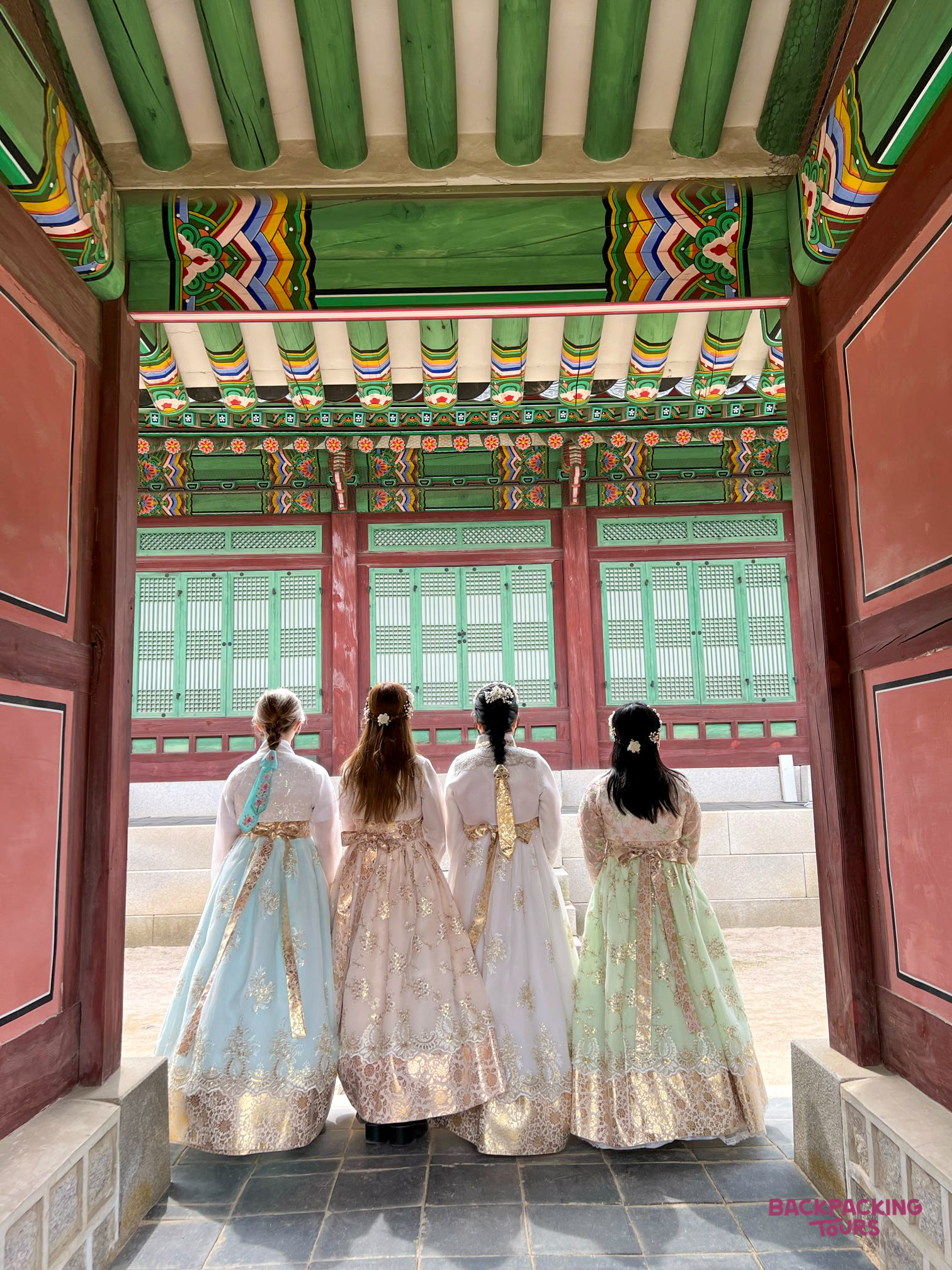 Four women in colorful hanbok dresses stand in a traditional Korean palace gateway in Seoul.
