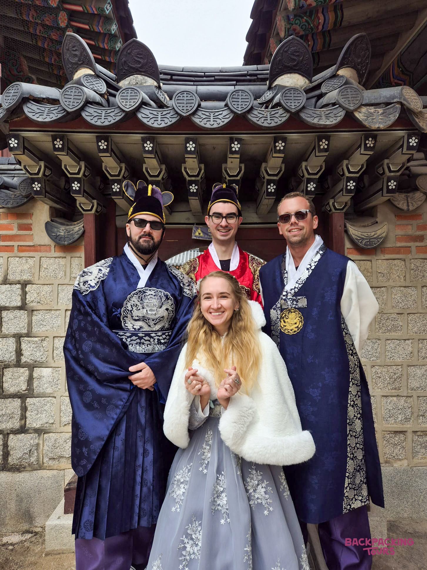 Four happy travelers pose in traditional hanbok at Gyeongbokgung Palace in Seoul.