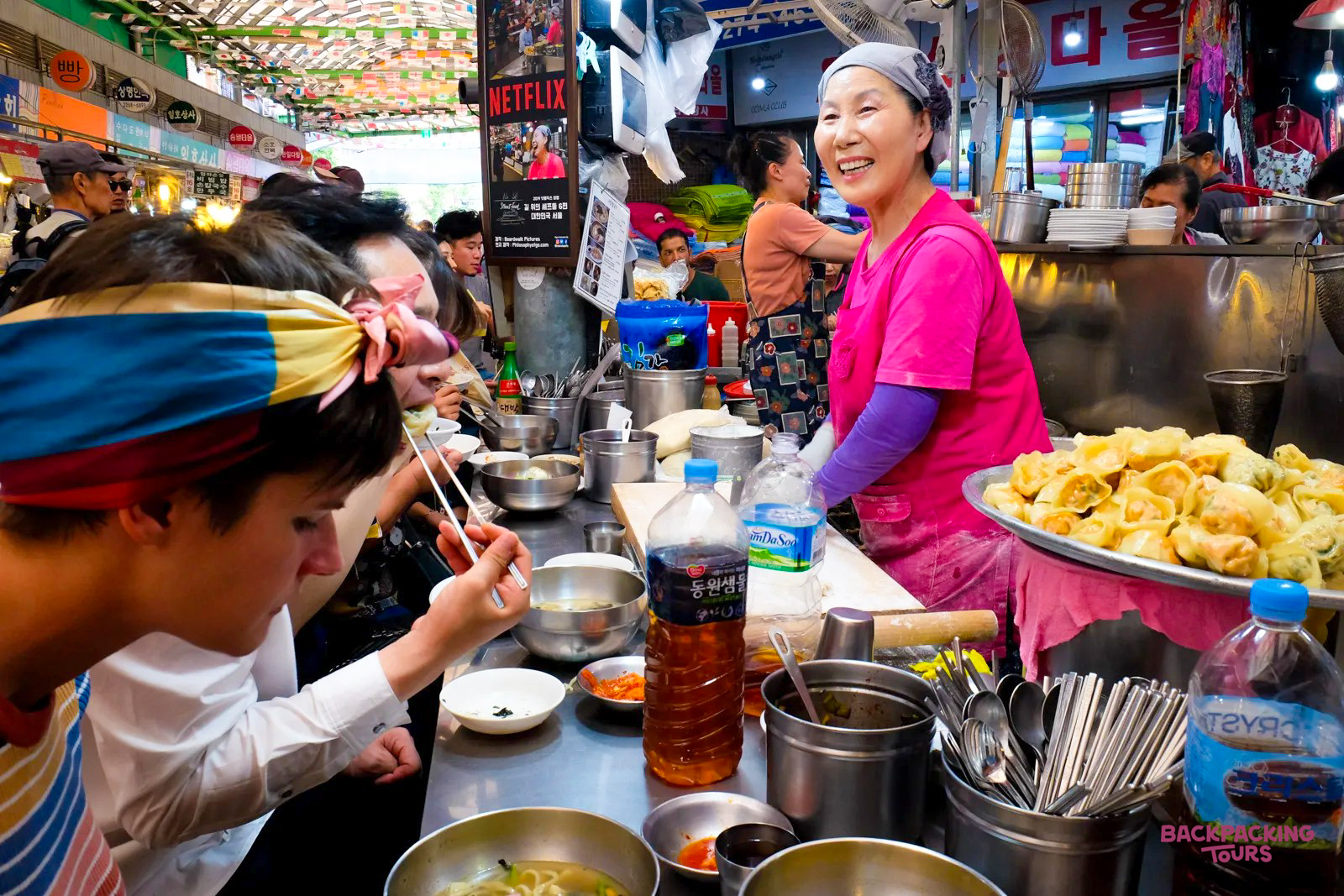 A smiling vendor serves delicious street food to travelers enjoying a lively market in Seoul.