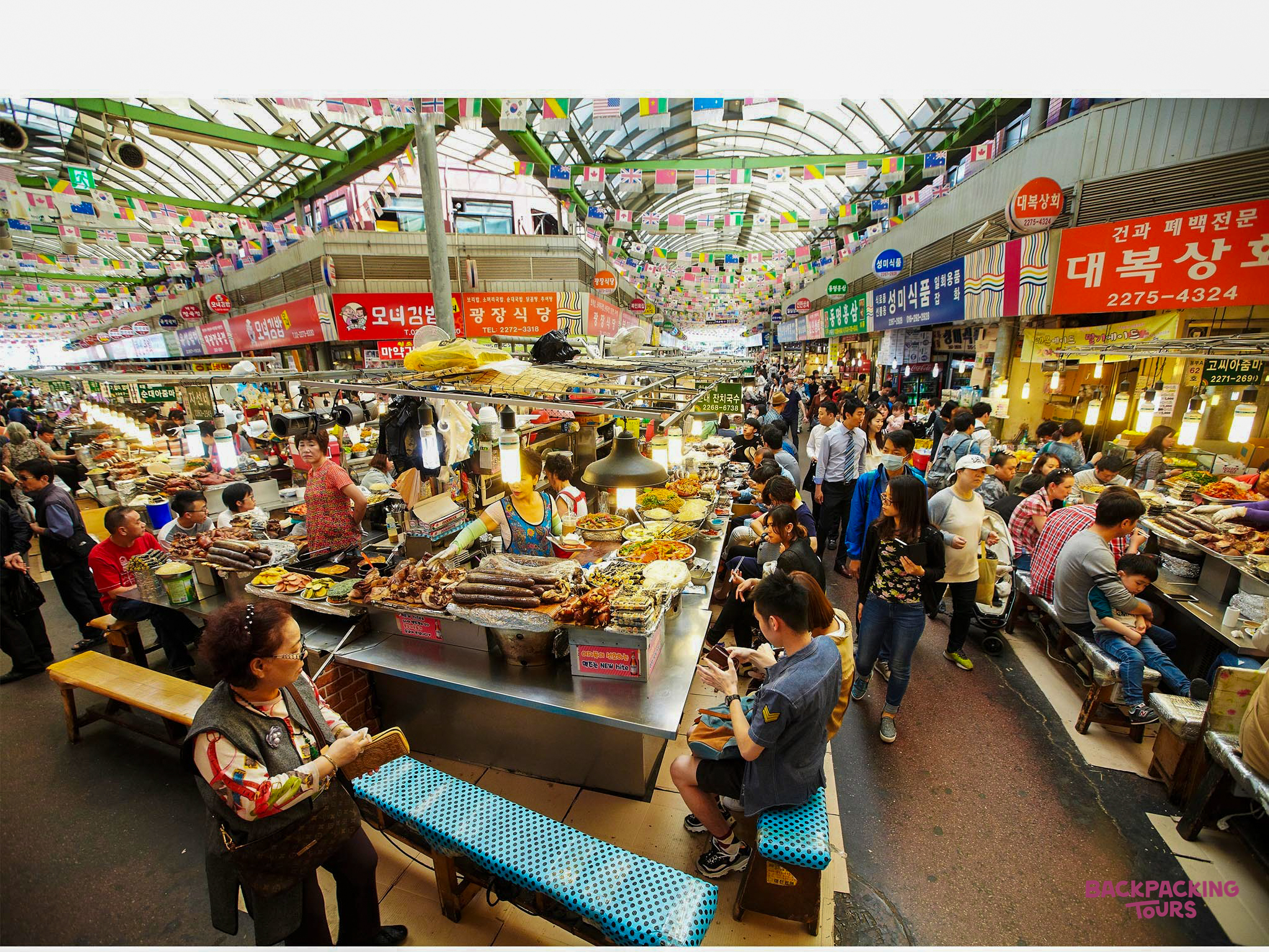 A vibrant Gwangjang Market in Seoul, bustling with people enjoying various Korean street foods.
