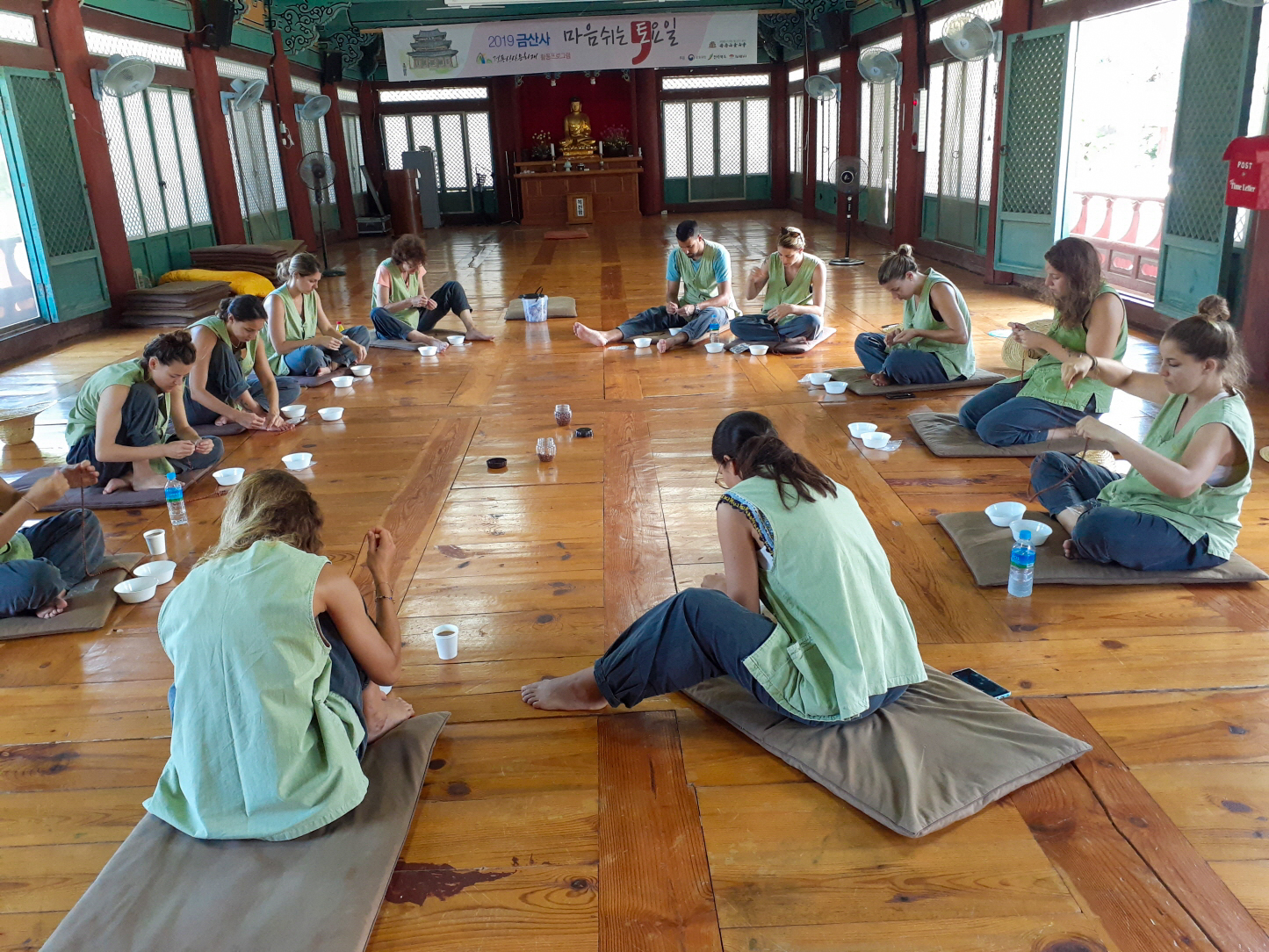 Travelers in green tops sit on mats, meditating in a serene traditional temple hall at Geumsunsa.
