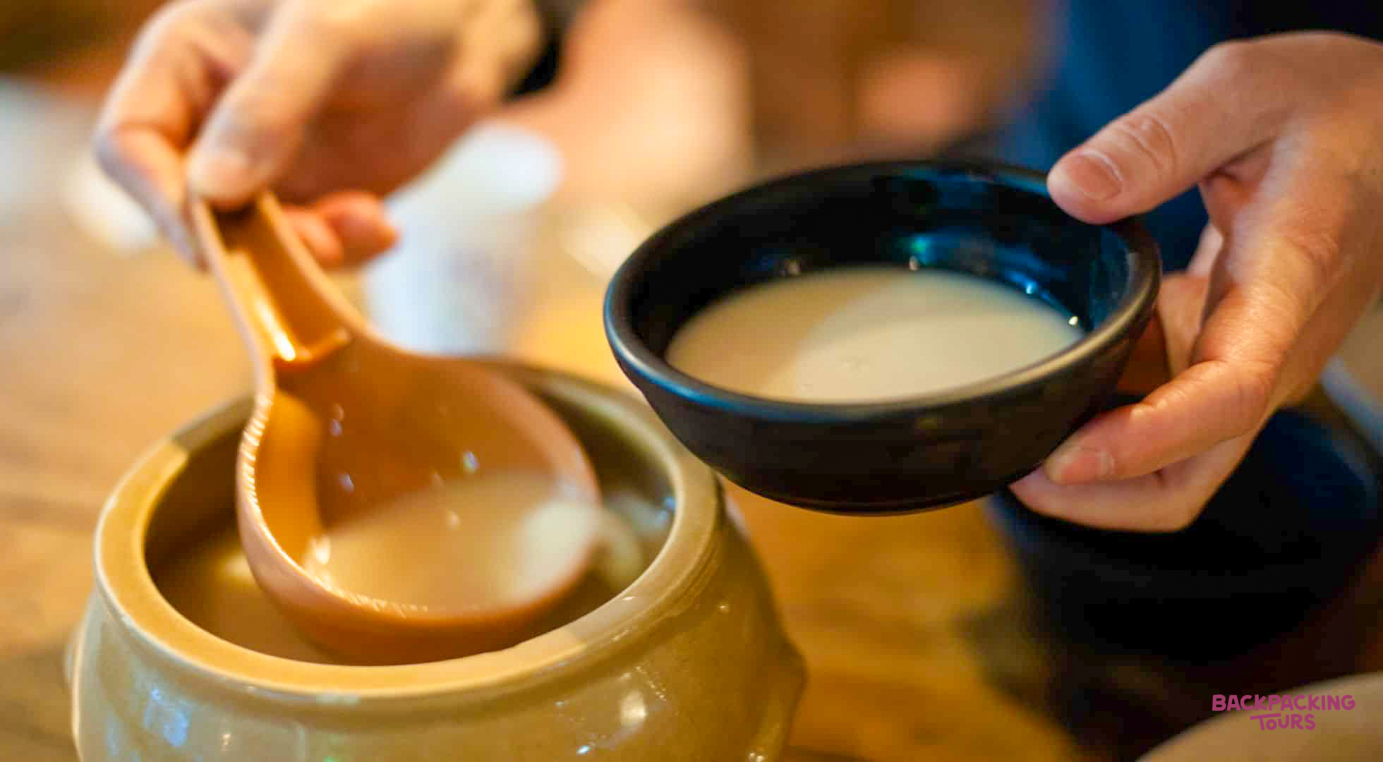 Pouring milky makgeolli from a traditional earthenware pot into a bowl during a tasting in Jeonju.