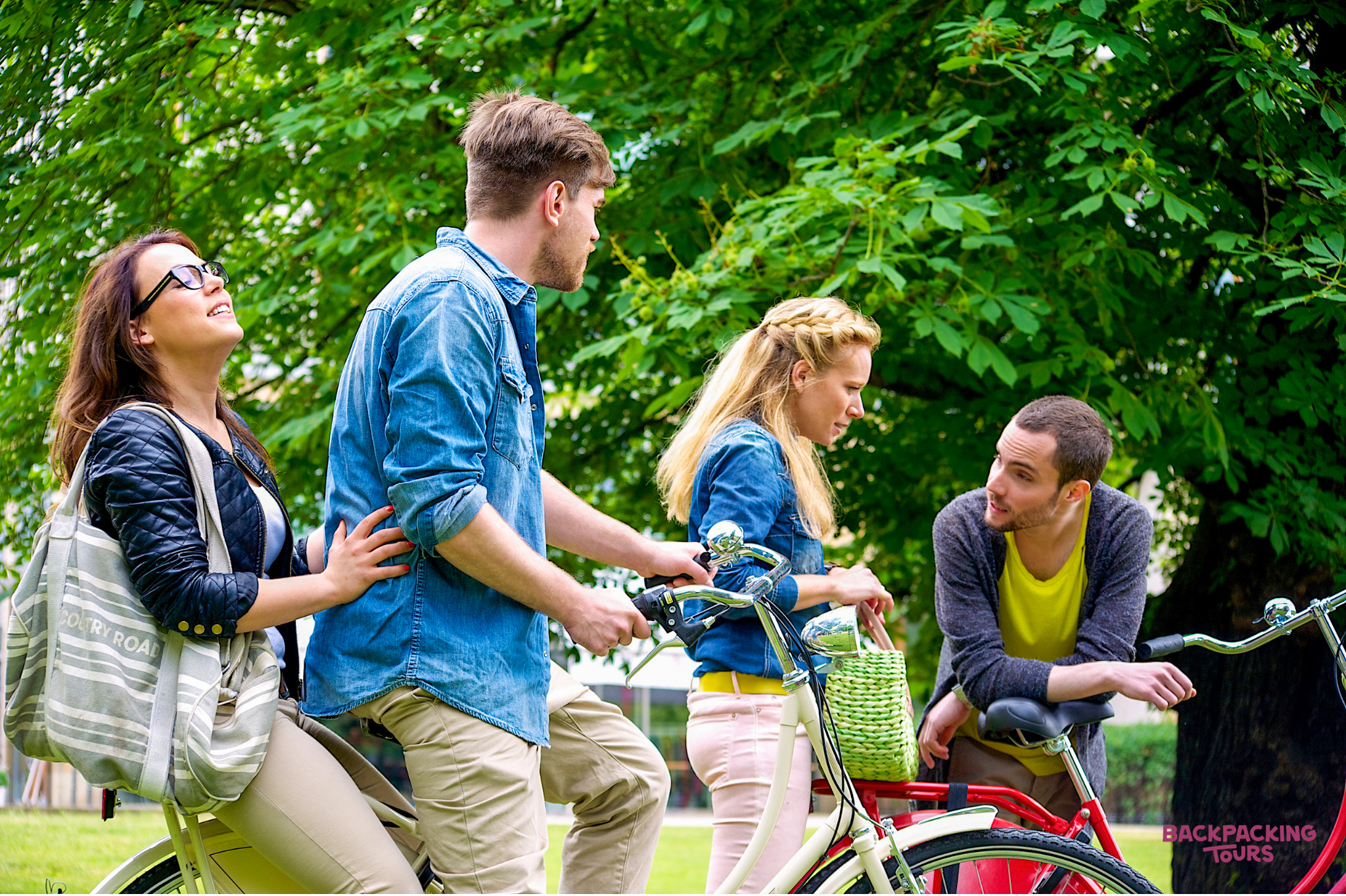 Four young travelers on a bike tour, chatting and enjoying the park scenery.