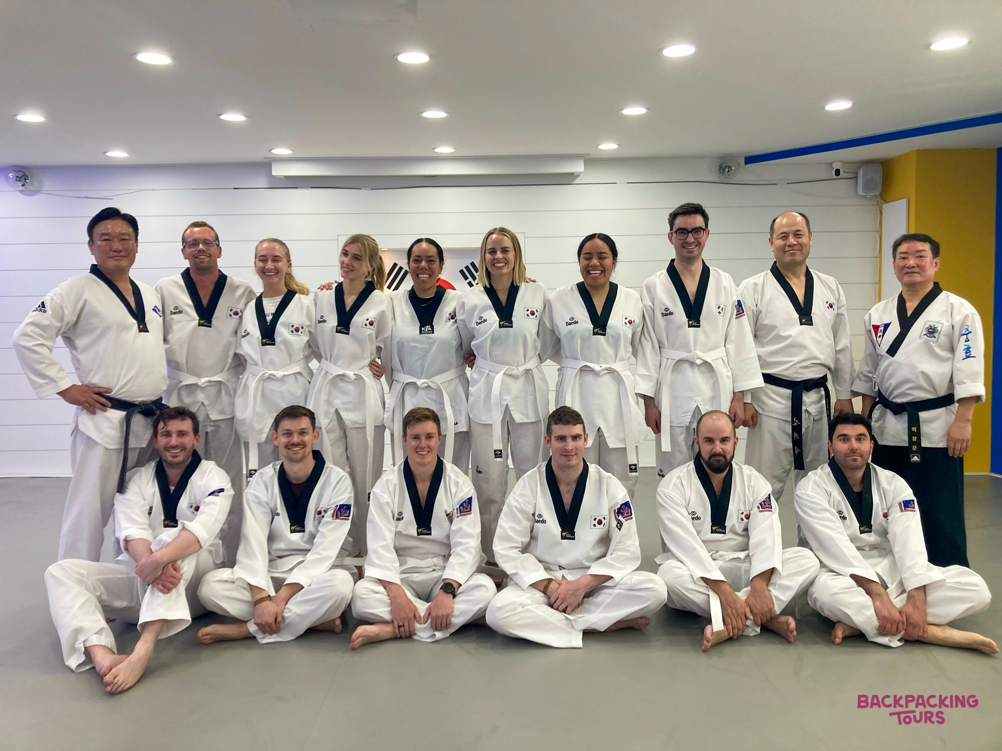 A group of travelers and instructors in white taekwondo uniforms posing after a class in Gyeongju.