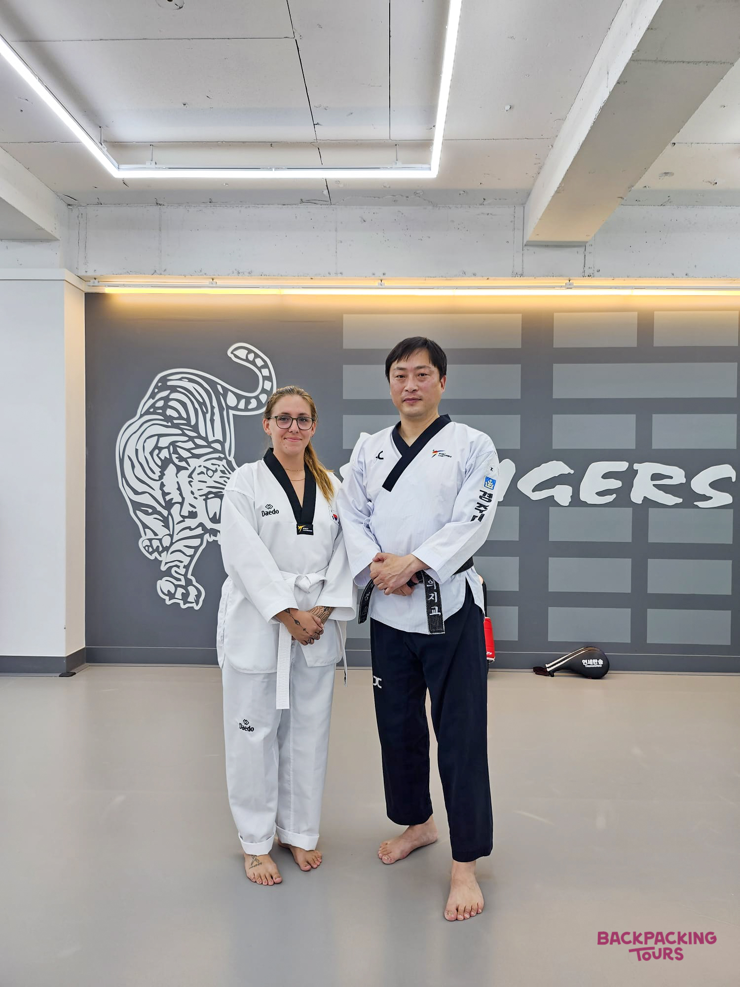 A woman and a Taekwondo instructor in doboks pose proudly in a Gyeongju dojang.