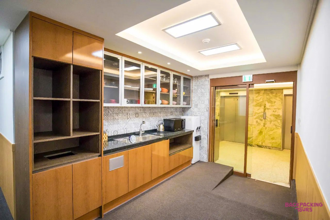 A clean and modern shared kitchen area with wooden cabinets and an elevator in a Seoul hostel.