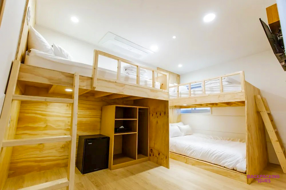 A clean, modern hostel room in Seoul with two wooden bunk beds and white bedding.