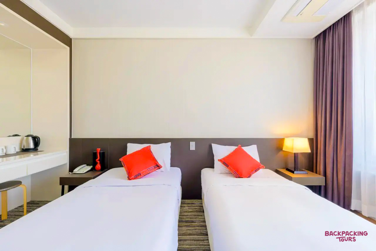 A comfortable and modern twin room with two single beds and orange pillows on Jeju Island.