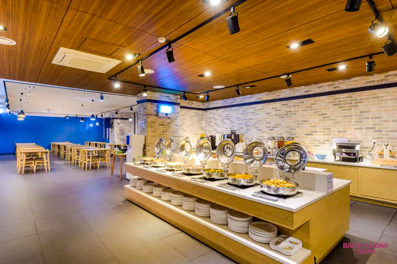 A bright, modern hotel breakfast buffet area with covered dishes and dining tables on Jeju Island.