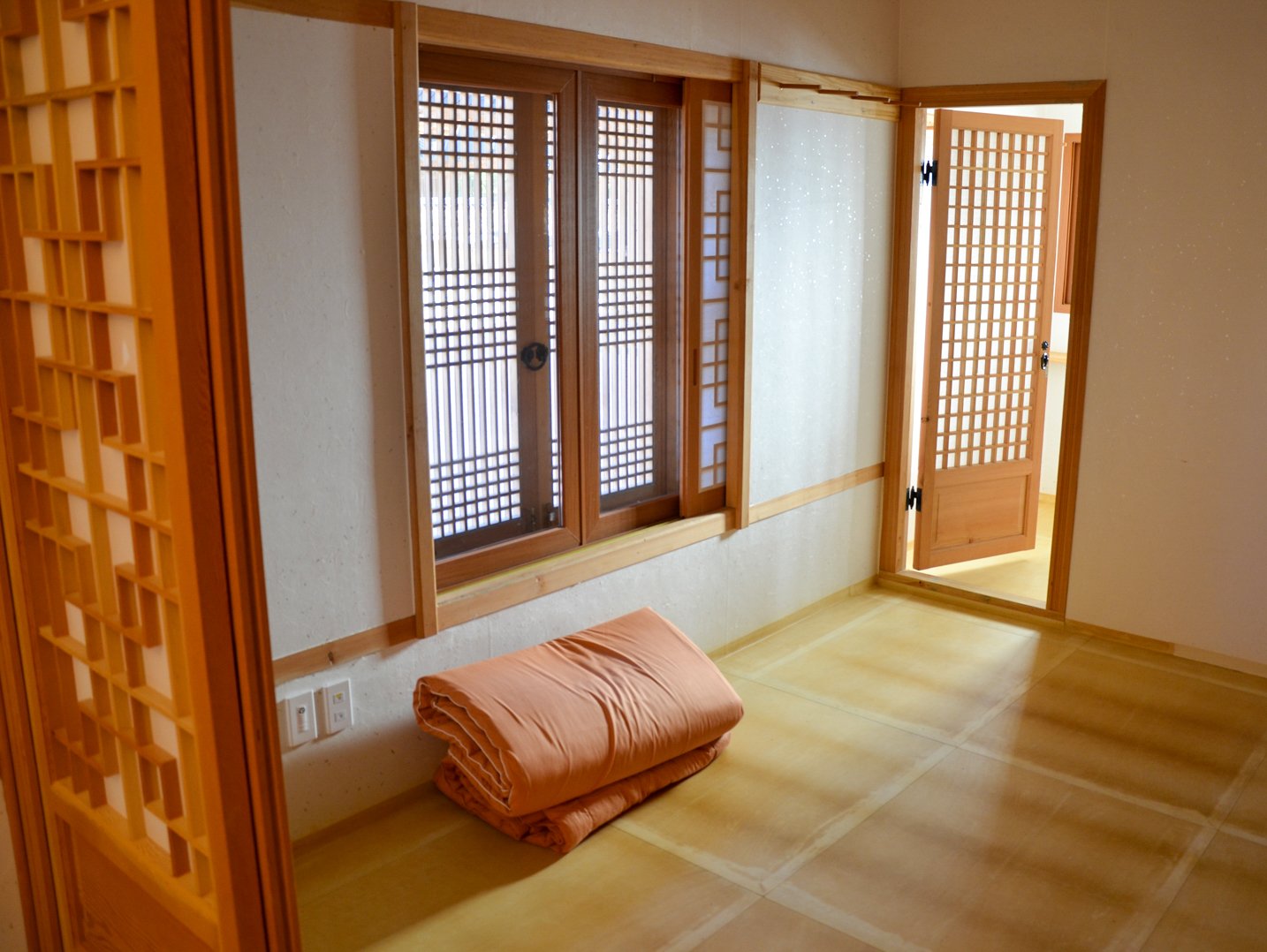 A serene traditional Korean temple room with wooden lattice windows and a folded blanket on the floor.