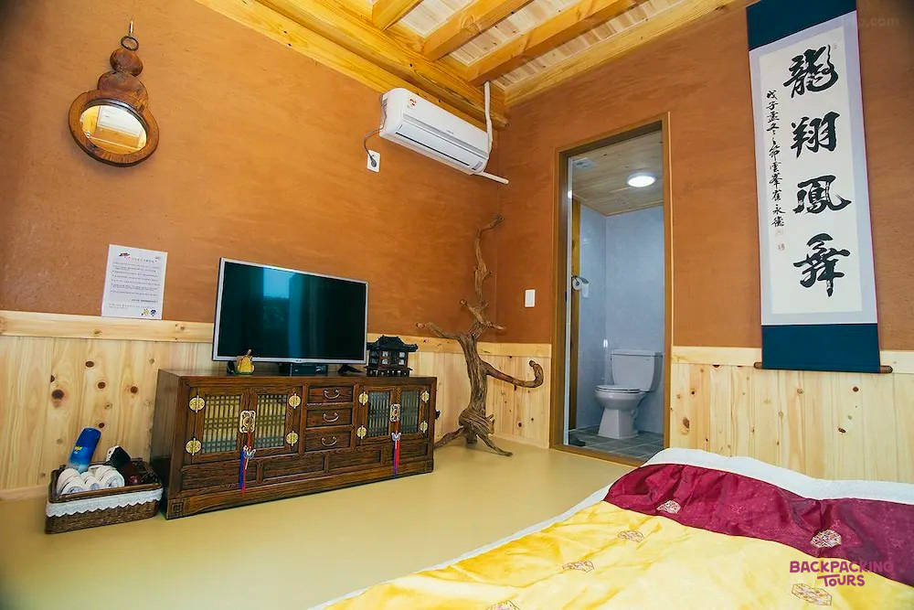 A cozy room in a traditional Hanok guesthouse in Jeonju, featuring a TV, ornate furniture, and a colorful quilt.