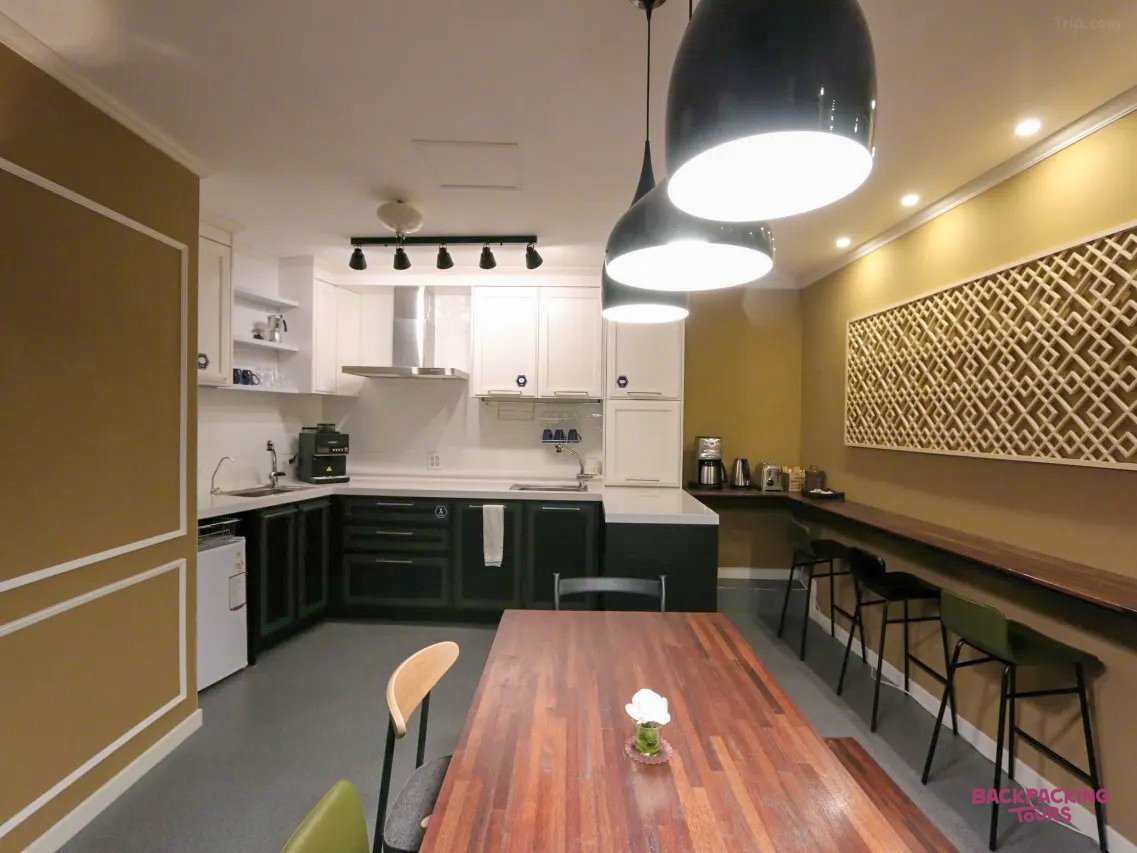 Contemporary hostel kitchen with dark green cabinets, wooden table, and bar area in Gyeongju.