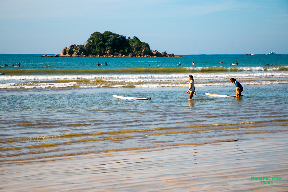 Two people with surfboards wading in the gentle waves at Mirissa beach, Sri Lanka.