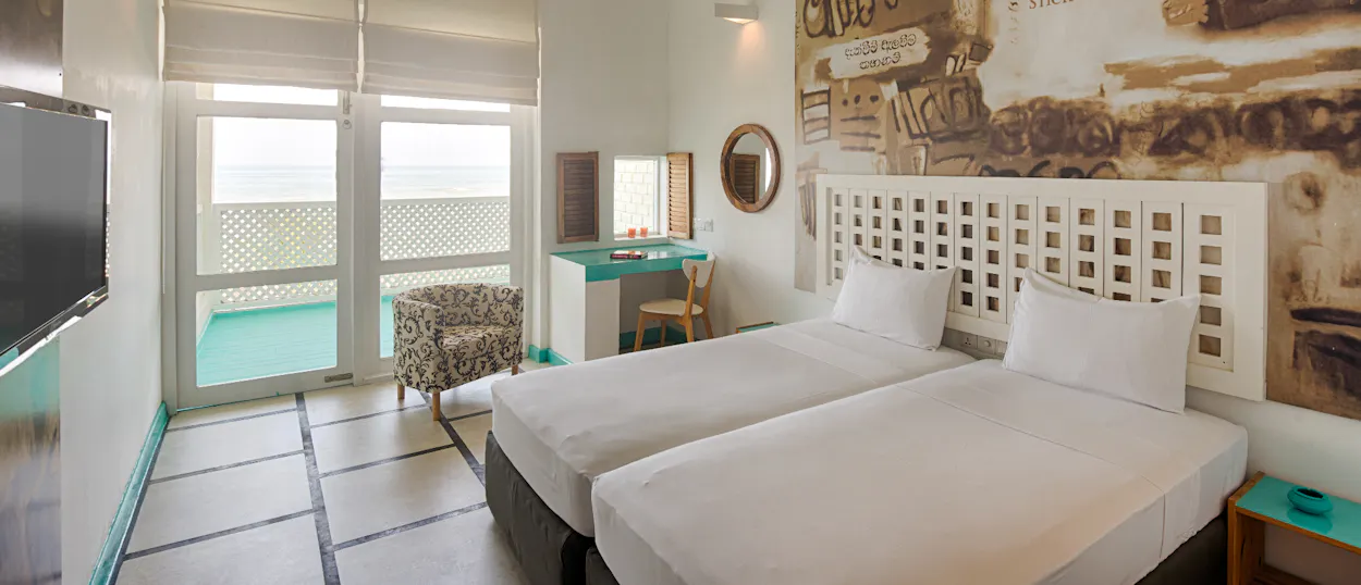 A modern hotel room in Colombo featuring two single beds and a balcony with an ocean view.