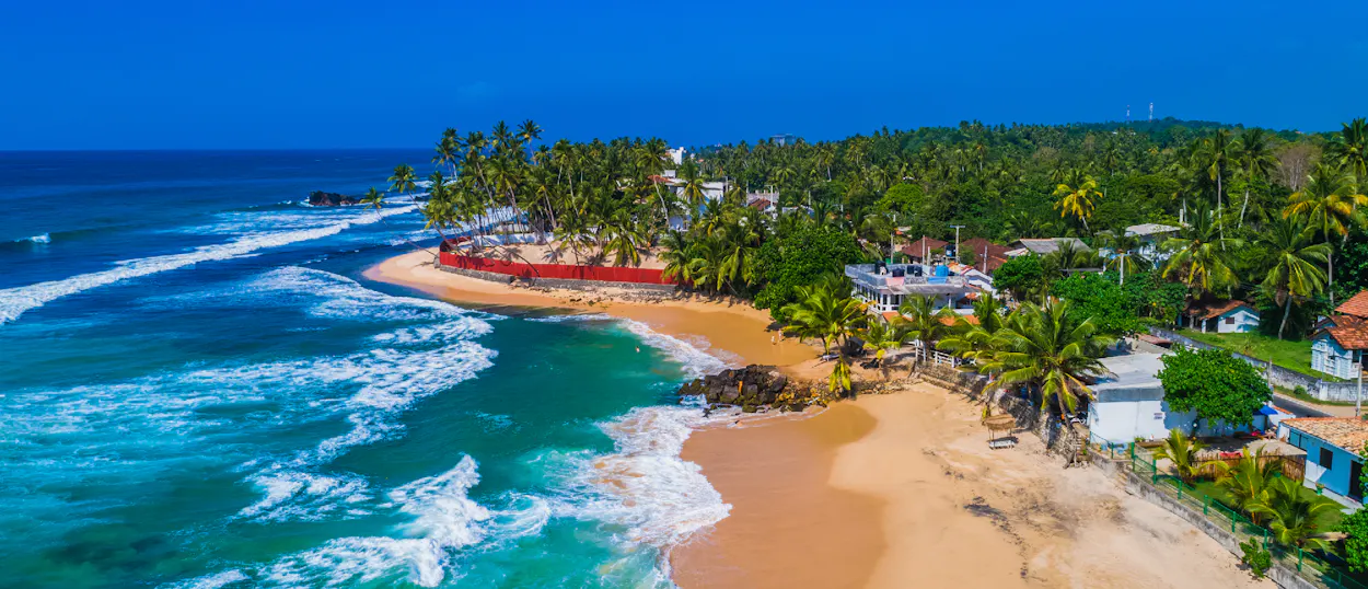 Stunning aerial view of a Sri Lankan beach with turquoise water, golden sand, and many palm trees.
