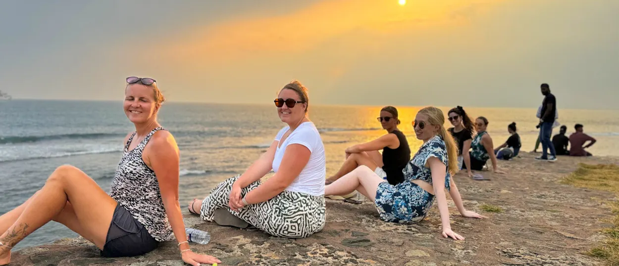 Smiling travelers sit on a rocky edge enjoying a beautiful sunset over the ocean in Weligama.