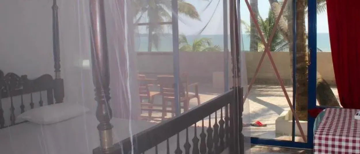 Cozy bedroom with a netted four-poster bed and a balcony view of the Weligama beach.