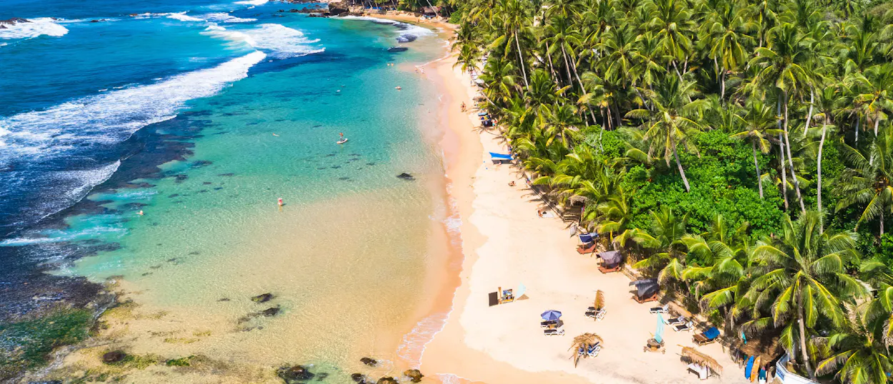 Aerial view of a beautiful sandy beach with clear turquoise water and lush palm trees in Unawatuna.