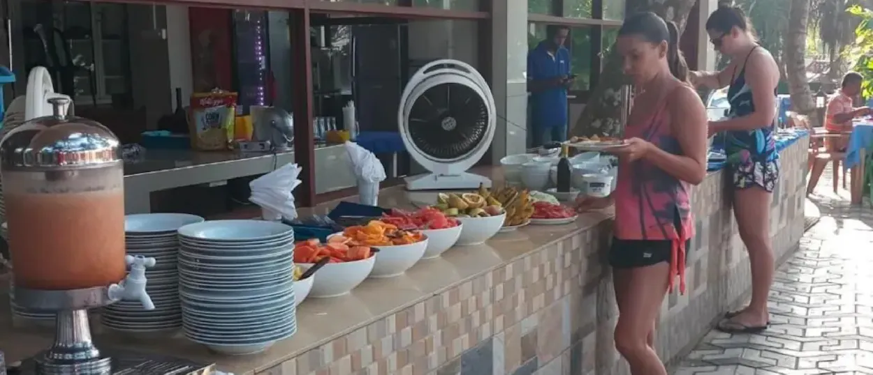 Two women serving themselves colorful fresh fruit from a breakfast buffet at a resort in Unawatuna.