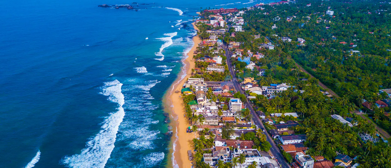 Vibrant aerial view of Unawatuna beach and town, with blue ocean waves and lush green vegetation.