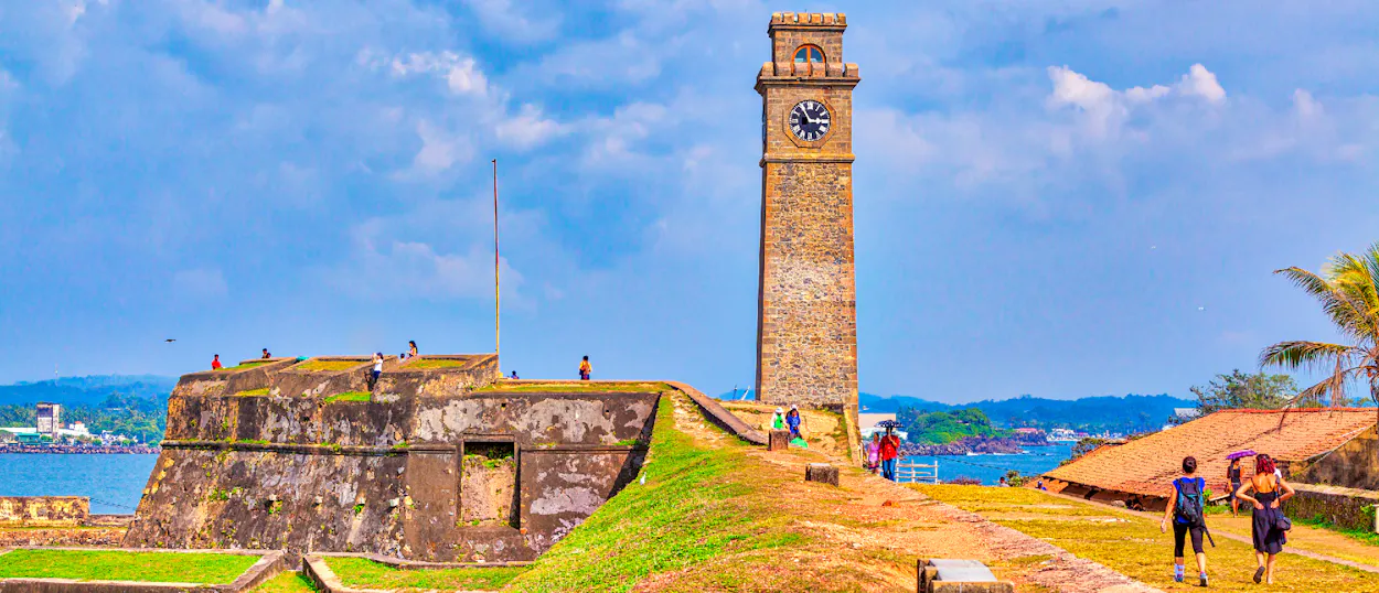 Visitors stroll along the historic Galle Fort walls and a prominent clock tower by the sea.