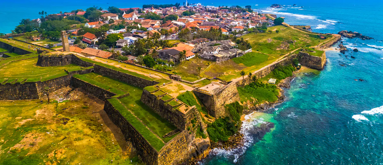 Aerial view of the historic Galle Fort in Sri Lanka, with green ramparts and a town by the turquoise ocean.