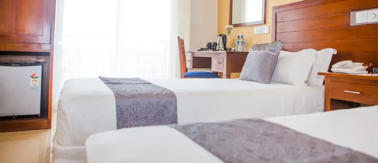 A bright and clean hotel room with two beds, a desk, and a mini-fridge.