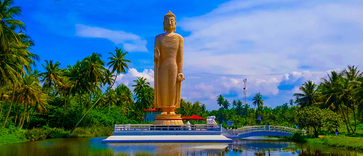 A majestic golden Buddha statue stands tall amidst palm trees and serene waters in Sri Lanka.