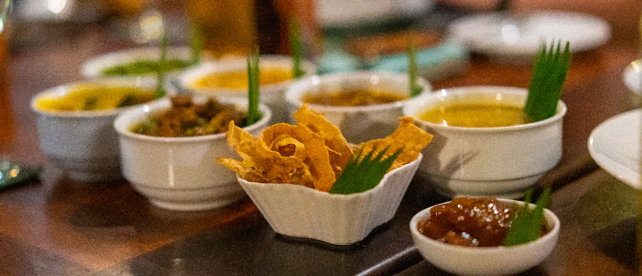 Small white bowls filled with colorful Sri Lankan curries and crispy snacks at a welcome dinner.