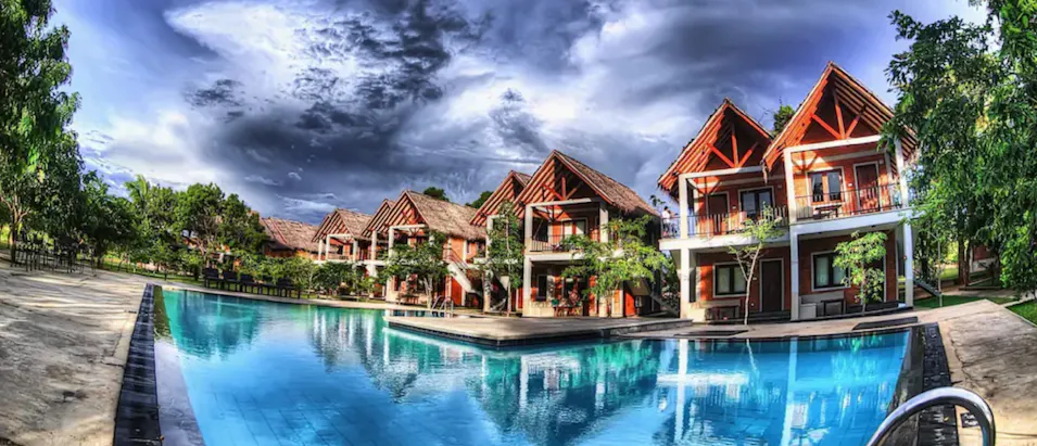 Beautiful resort bungalows with a large swimming pool reflecting a dramatic cloudy sky in Sri Lanka.