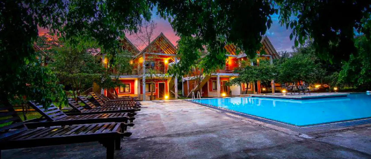 A beautiful resort pool area with lounge chairs and illuminated buildings at dusk in Sigiriya, Sri Lanka.