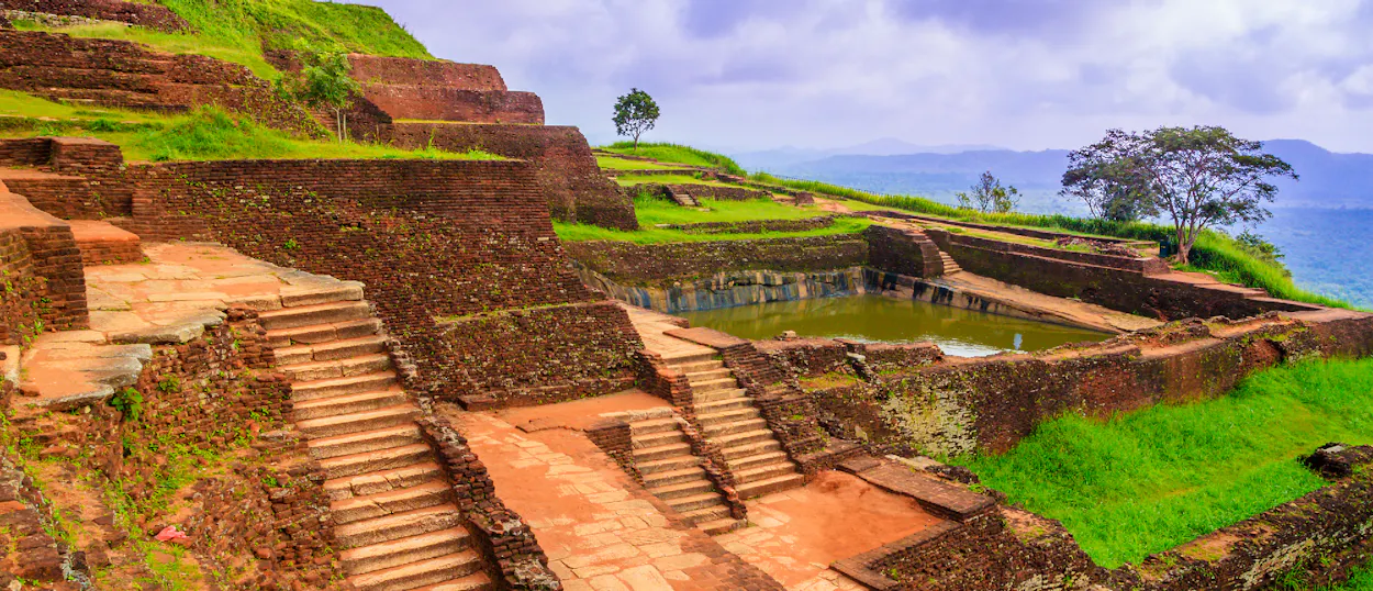 Ancient brick ruins with terraced steps, green lawns, and a tranquil pool at Sigiriya, Sri Lanka.