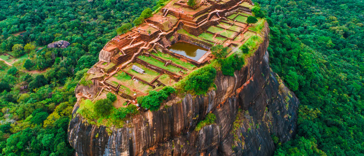 Sigiriya Rock, an ancient fortress with terraced gardens and a pond, rising from a dense forest.