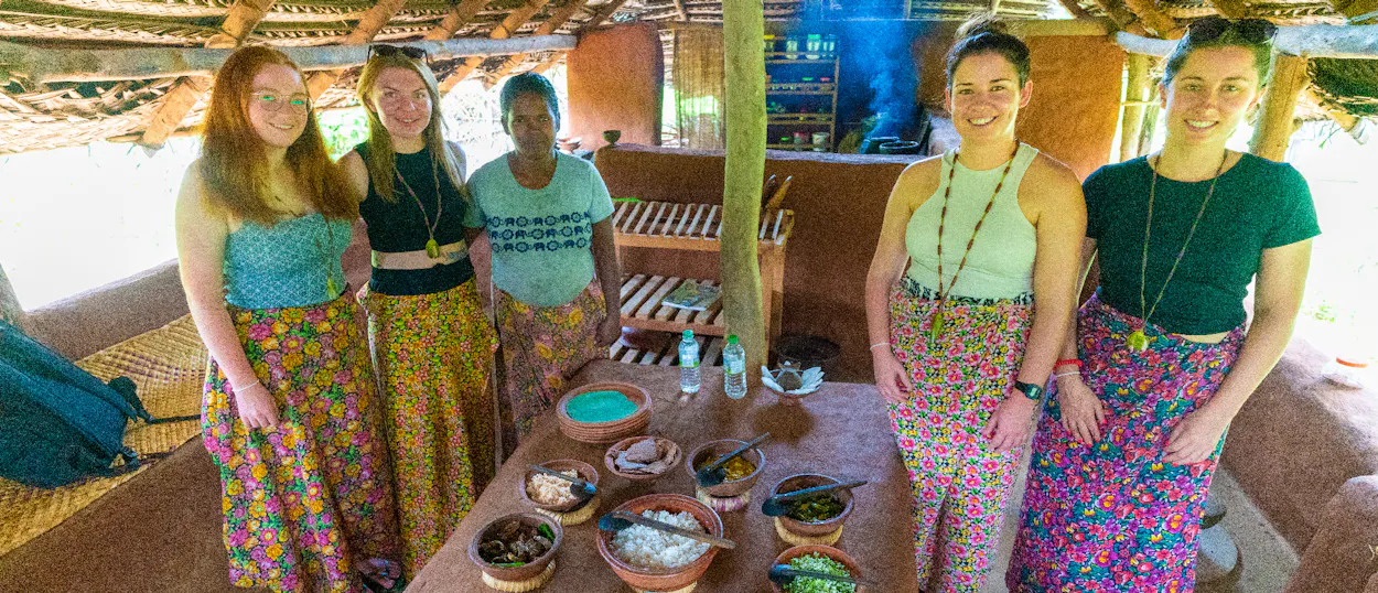 Happy tourists and local women sharing a traditional Sri Lankan meal in a rustic village kitchen in Sigiriya.