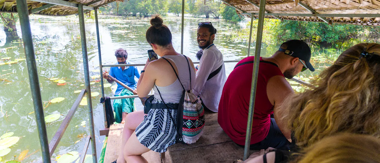 Happy tourists on a traditional boat exploring a serene lake with lily pads in Sigiriya.