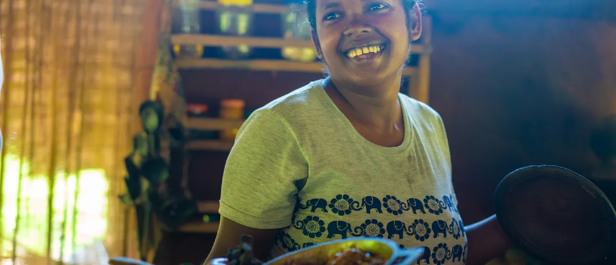 A smiling woman in a local Sri Lankan village holds a pan of authentic curry.