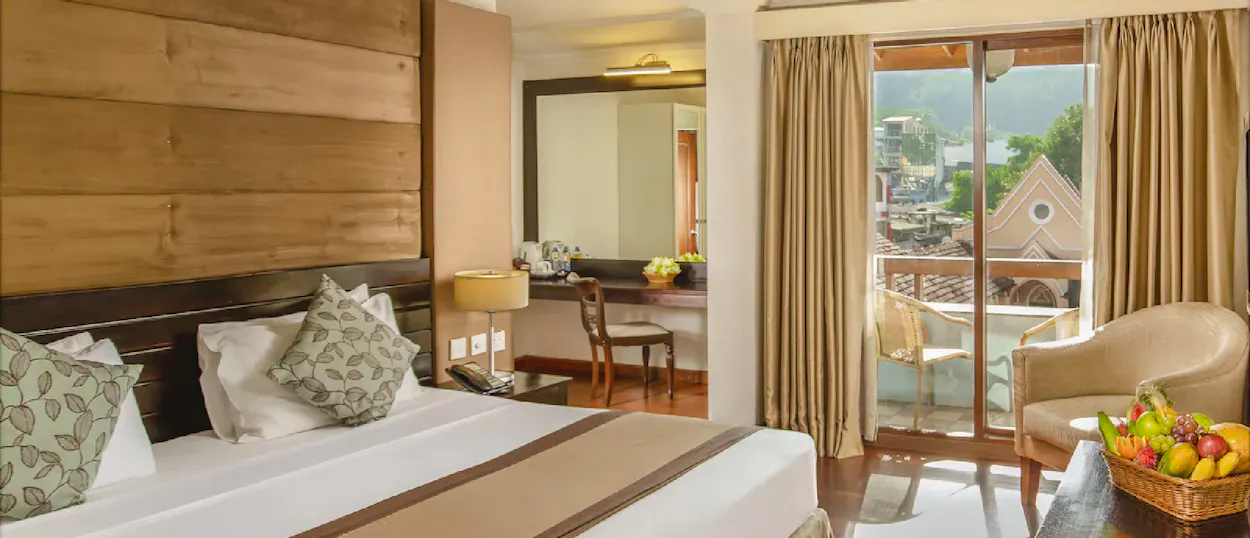 A comfortable hotel room in Kandy with a large bed, fruit basket, and balcony view.