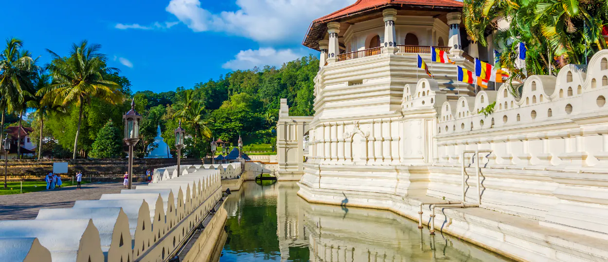 Majestic white temple with a red roof and moat in Kandy, Sri Lanka, under a blue sky.