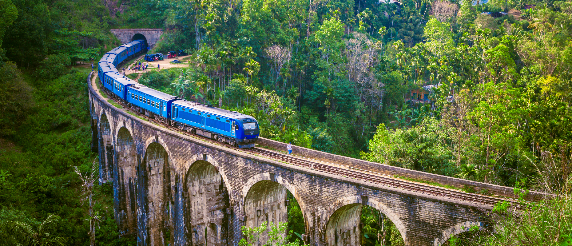 A blue train crosses the iconic Nine Arch Bridge in Ella, surrounded by lush green Sri Lankan jungle.